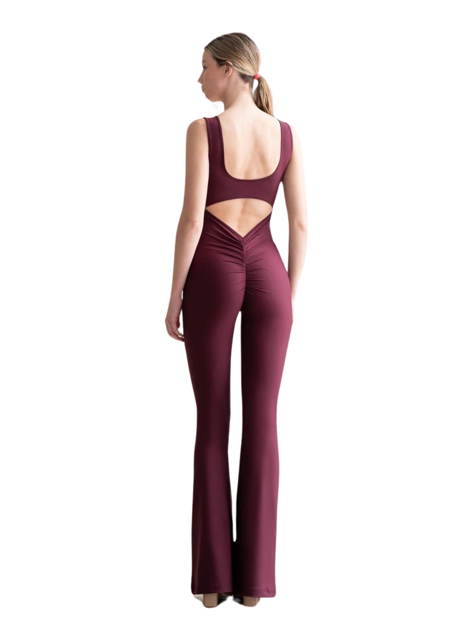 Eine Frau, die einen Lismina 1501 Scrunch Butt Jumpsuit in Dunkelviolett trägt, steht vor einem weißen Hintergrund.